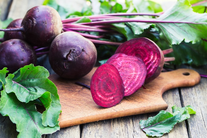 Beets with leafy greens on a cutting board