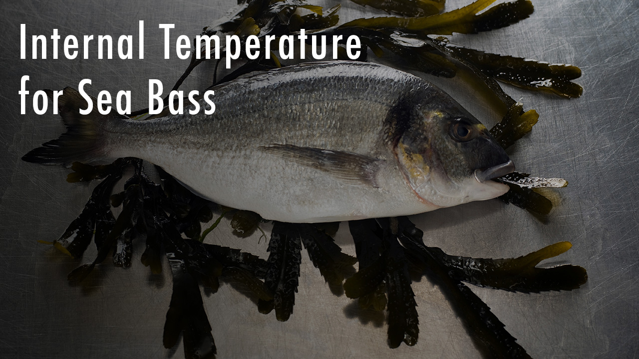 Whole raw sea bass placed on seaweed over a metal surface, with text overlay reading 'Internal Temperature for Sea Bass'